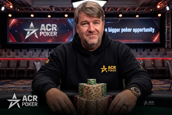 Chris Moneymaker sitting behind a chip stack in ACR Poker branded kit at a tournament table