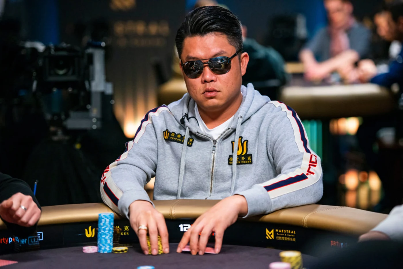 Ivan Leow in a Triton Poker jacket and sunglasses behind his chips at a Triton final table