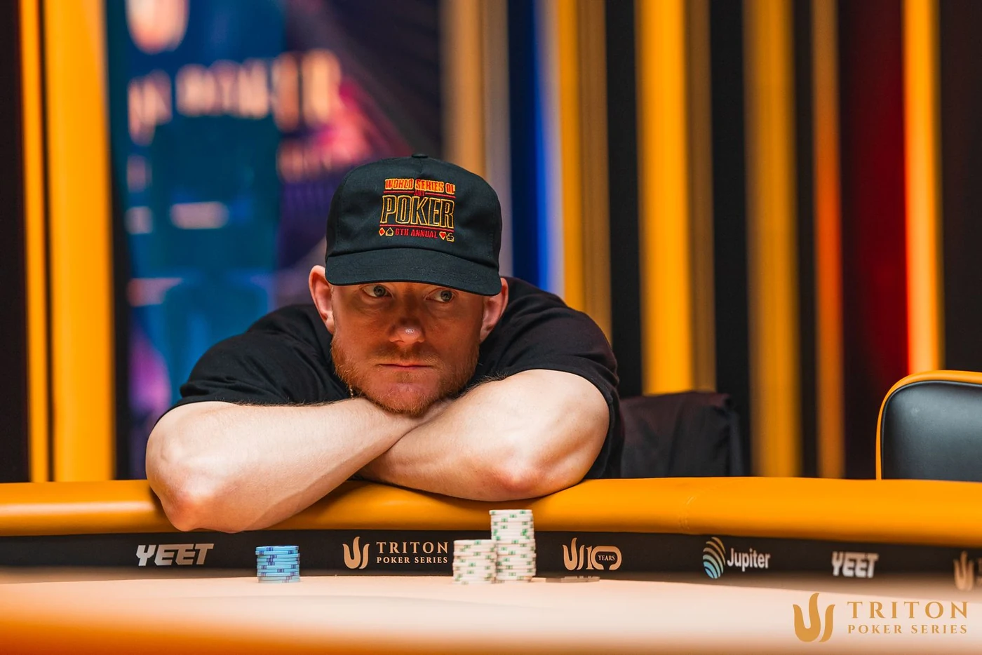 Jason Koon resting on his arms behind two chip stacks at a Triton Poker Series table