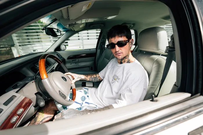 Mikki Mase sitting in a car wearing sunglasses and a white shirt