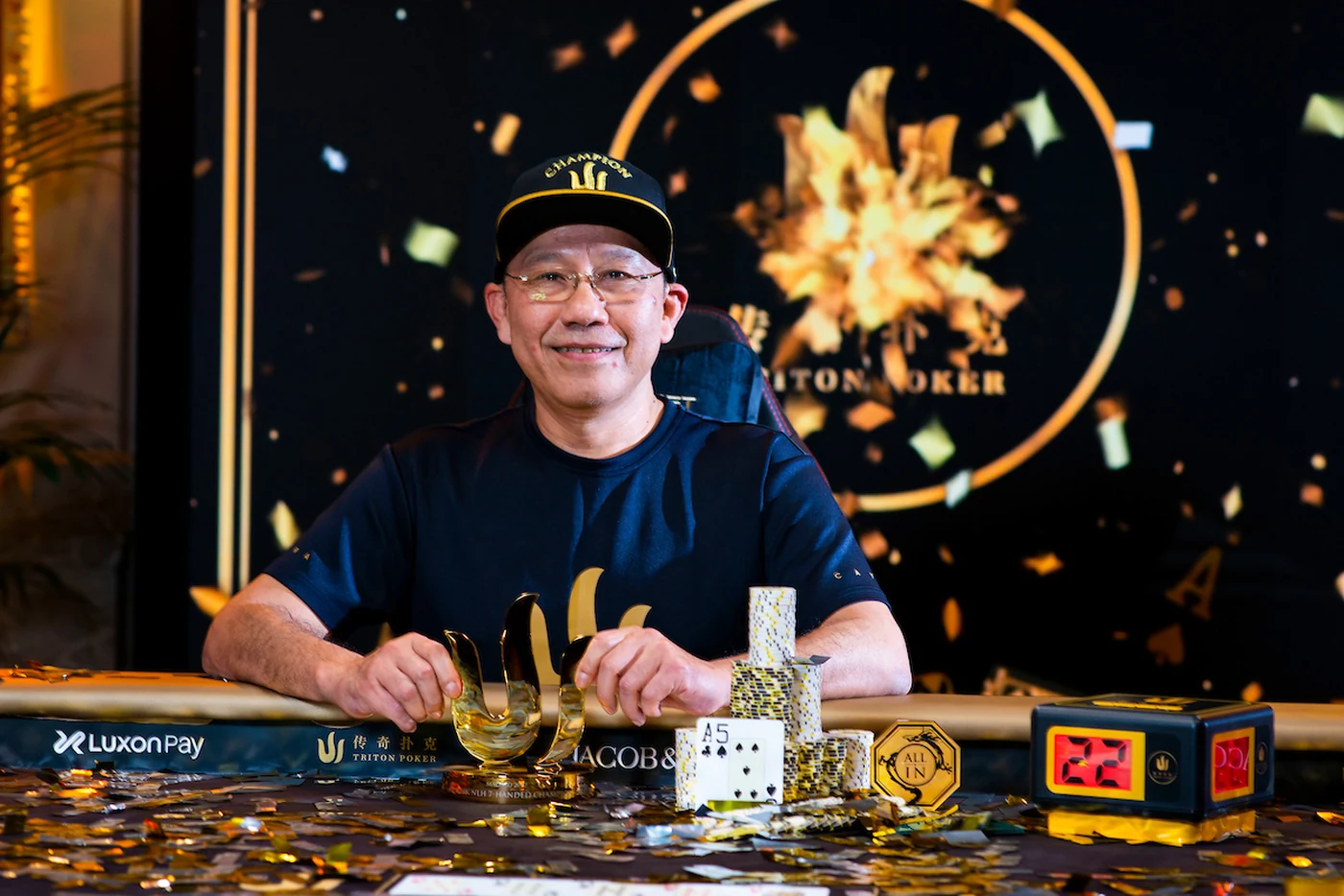 Paul Phua seated behind the gold Triton Poker Series trophy as confetti falls