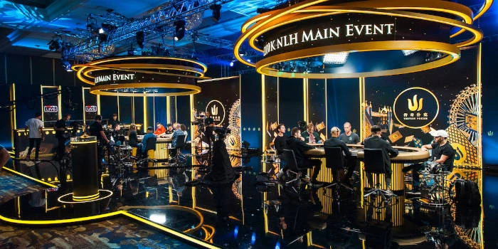 Players seated at the Triton Poker Main Event feature table under gold ring lighting