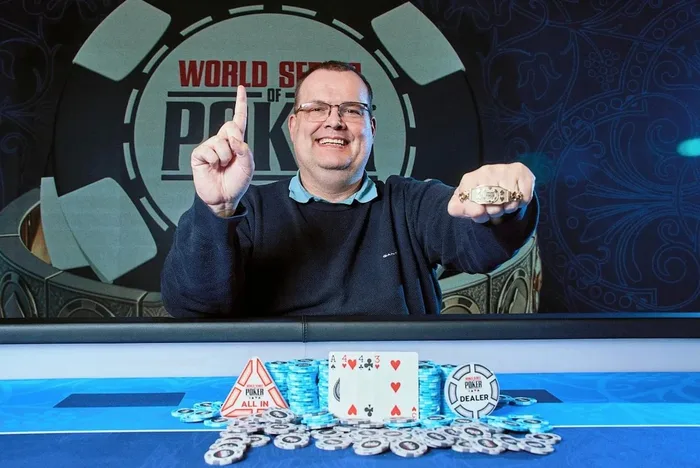 Frank Koopmann WSOP Europe 2026 first bracelet winner Frank Koopmann holding up his WSOP Europe 2026 bracelet with his winning A-4-4-3 hand displayed at the Hilton Prague