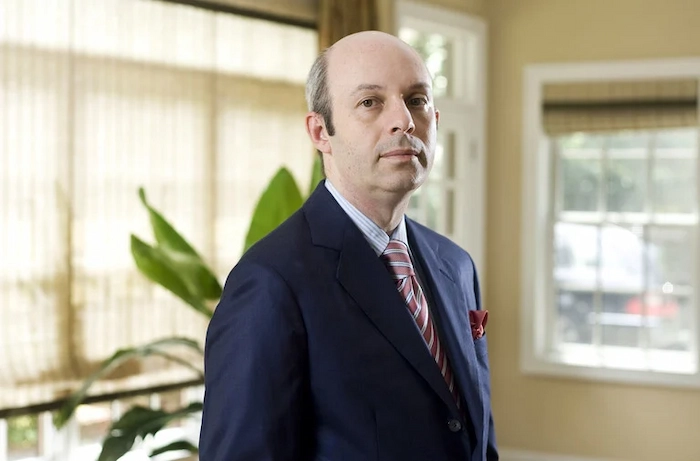 Tom Goldstein, prominent U.S. Supreme Court litigator and SCOTUSblog founder, standing in a formal office setting wearing a navy suit, light blue striped shirt, red-and-white striped tie, and red pocket square, with a serious expression.