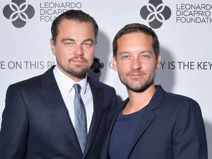 Tobey Maguire and Leonardo DiCaprio Tobey Maguire and Leonardo DiCaprio posing together on the red carpet at a Leonardo DiCaprio Foundation event, both in dark suits with Tobey in a blue tie and Leo in a gray one, standing in front of the foundation logo backdrop.