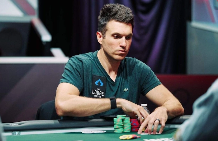 Doug Polk intense at The Lodge felt: green tee with logo, chip stacks in hand.