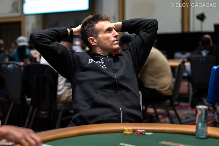 Doug Polk, 3x WSOP bracelet winner and high-stakes specialist, leaning back with hands behind head in black DOPE hoodie at the poker table during a live tournament session.